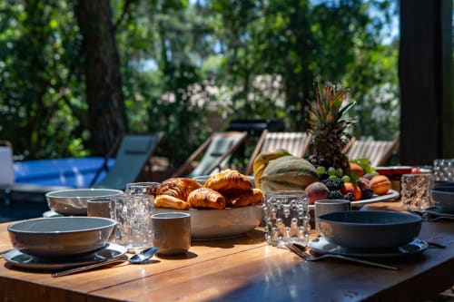Petit-déjeuner en plein air à la villa La Loge Du Bassin avec croissants frais, fruits, couverts et vue sur la piscine