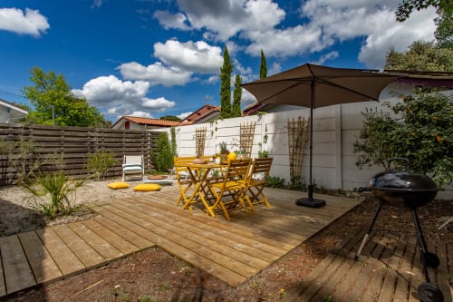 Terrasse ensoleillée de la villa La Palombière à Andernos-les-Bains avec chaises bistro jaunes, parasol et barbecue