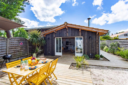 Villa La Palombière au Bassin avec table de salle à manger jaune, terrasse en bois, façade en bois foncé et vue sur le jardin