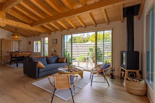 Salon moderne de la villa La Loge Du Bassin avec poutres en bois, canapé bleu, cheminée et vue sur le jardin à Andernos-les-Bains