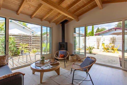 Séjour de villa moderne avec poutres apparentes en bois, poêle à bois, fauteuils en rotin et portes vitrées donnant sur