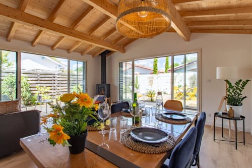 Salle à manger avec poutres en bois, table fleurie, cuisine moderne et vue sur le jardin à la villa La Palombiere