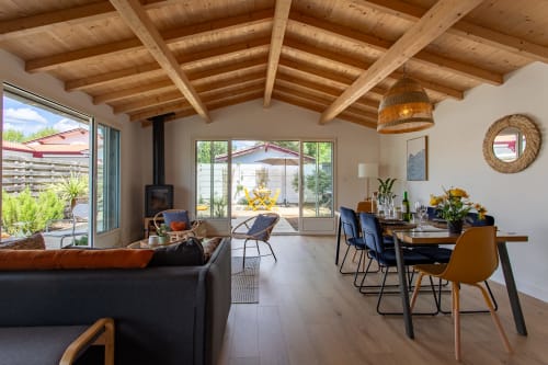 Séjour ouvert à La Loge Du Bassin avec plafond à poutres apparentes, table à manger, cuisine, canapé et vue sur le jardin