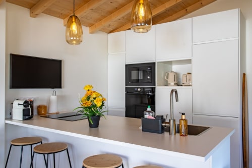 Cuisine blanche moderne avec îlot, fleurs jaunes et plafond aux poutres en bois à la villa La Palombière