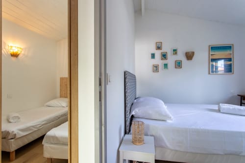 Chambre lumineuse à la villa La Loge Du Bassin à Andernos-les-Bains avec lits blancs, œuvres côtières encadrées et touches de bois