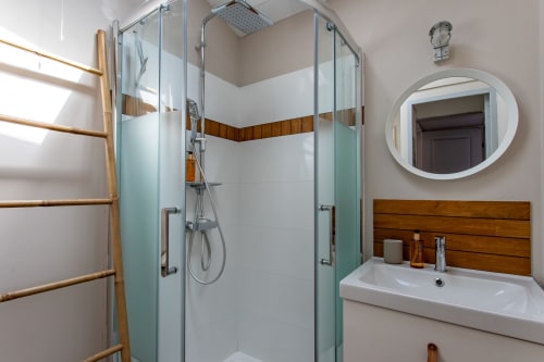 Salle de bains moderne avec douche vitrée, meuble vasque en bois et miroir rond à la Villa La Palombière à Andernos-les-Bains