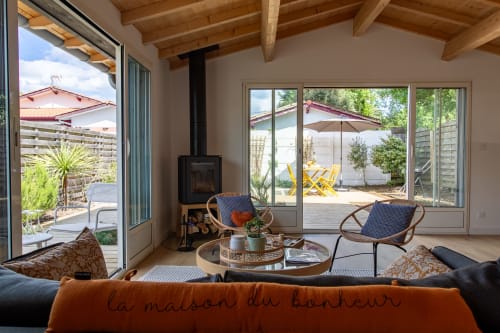 Intérieur de villa moderne à La Loge Du Bassin avec poutres en bois, cheminée et vue sur le jardin par portes vitrées sur patio