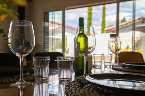 Table élégante dressée à la villa La Palombière avec verres à vin, bouteille verte et vue sur le jardin par les fenêtres