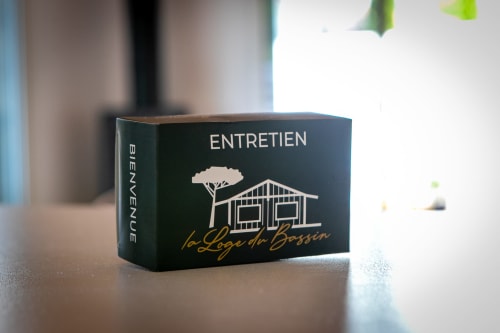 Boîte d'entretien La Loge du Bassin avec illustration de maison et logo d'arbre sur emballage noir