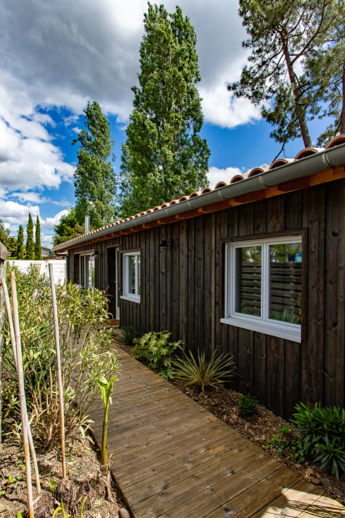 Villa contemporaine en bois foncé à La Loge Du Bassin, fenêtres à cadre blanc, terrasse en bois, peupliers élancés et jardin