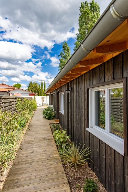 Villa contemporaine en bois sombre avec terrasse en bois, fenêtres à cadre blanc et vue sur le jardin à La Loge Du Bassin
