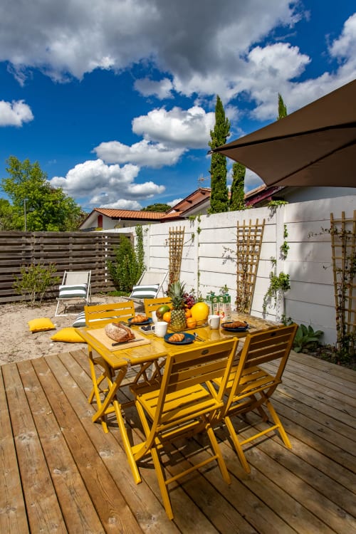 Salle à manger jaune en plein air sur terrasse en bois à la villa La Palombière à Andernos-les-Bains, avec mets et centre de table en ananas