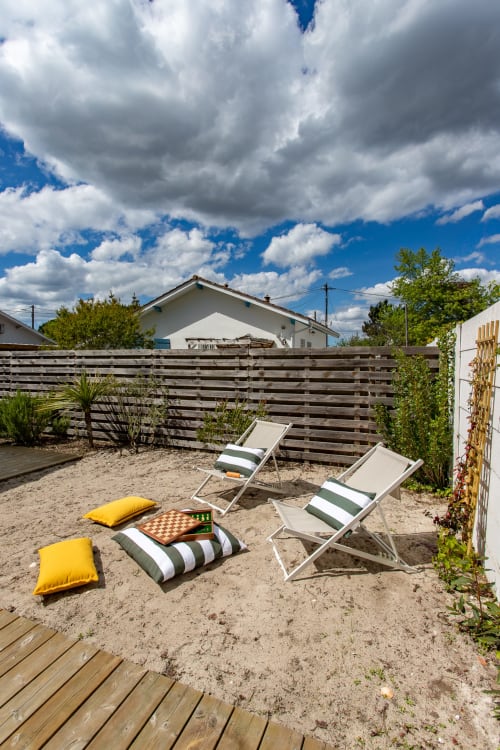 Terrasse sur plage de sable avec transats rayés, coussins jaunes et échiquier à la villa La Loge Du Bassin, Andernos-les-Bains