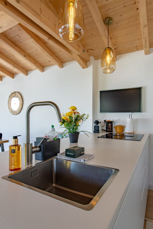 Évier moderne avec robinet en acier inoxydable, plan de travail blanc, plafond à poutres apparentes et luminaires suspendus à La Palombière