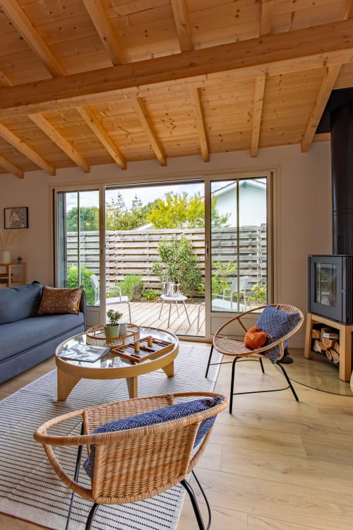 Séjour villa moderne à La Loge Du Bassin avec poutres bois, fauteuils en rotin, canapé bleu et vue sur jardin terrasse