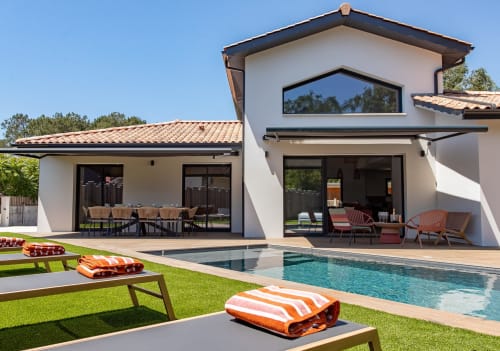 Vue de la piscine de la Villa La Parenthèse avec chaises longues, piscine chauffée et maison blanche moderne avec terrasse à La Loge Du