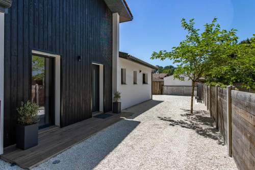 Cour moderne de la villa La Loge Du Bassin à Andernos-les-Bains avec bois noir, murs blancs et patio de graviers