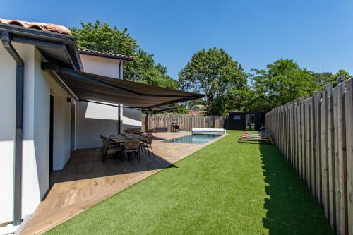 Jardin de Villa la Parenthese avec piscine chauffée, pelouse verdoyante, terrasse en bois, chaises longues et store moderne à La Loge Du