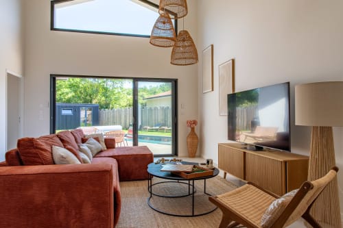 Salon contemporain de villa avec canapé rouge, meuble TV en bois et vue sur la piscine par les portes vitrées de La Parenthèse
