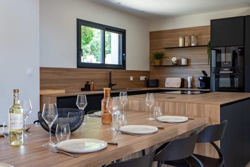 Cuisine et salle à manger modernes à la Villa la Parenthèse à Andernos-les-Bains avec plans de travail en bois, électroménagers noirs et salle à manger
