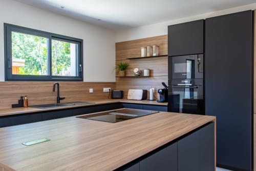 Cuisine moderne avec plans de travail en bois, armoires noires et appareils en acier inoxydable à Villa la Parenthese