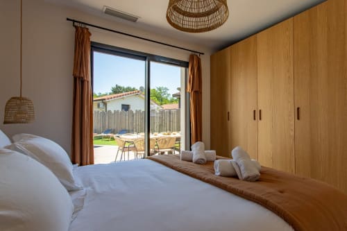 Chambre moderne avec armoire en bois, literie blanche et portes vitrées donnant sur la vue de la piscine du jardin à Villa la Parenthese,