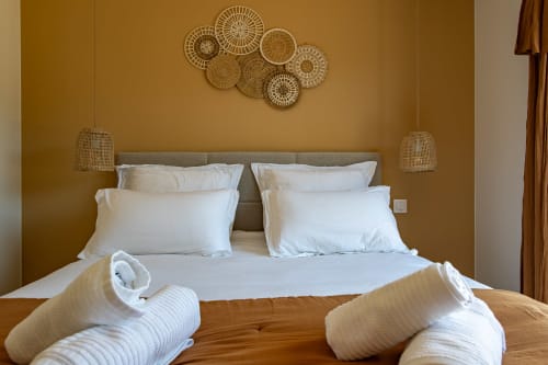 Chambre luxueuse à La Loge Du Bassin avec oreillers blancs, tête de lit beige et luminaires suspendus tissés à Andernos-les-Bains