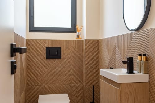 Salle de bain moderne à la Villa la Parenthèse avec carrelage imitation bois chevron, fixtures noirs, lavabo blanc et miroir rond