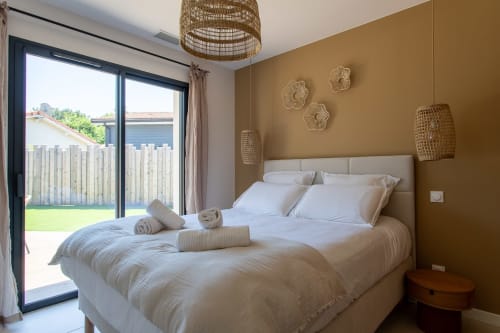 Chambre moderne à La Loge Du Bassin avec literie blanche, mur d'accent doré, décoration tissée et portes sur jardin