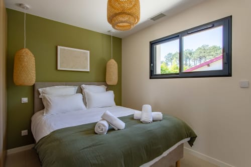 Chambre moderne à Villa la Parenthese avec mur d'accent vert olive, linge blanc, luminaires tissés et vue sur le jardin