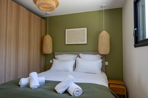 Chambre moderne avec mur d'accent vert olive, luminaires suspendus tissés, literie blanche, serviettes roulées à la villa La Loge Du Bassin