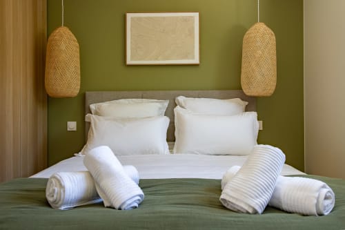 Chambre de villa contemporaine aux murs vert olive, linge blanc, serviettes roulées et luminaires en suspension tissés à La Loge Du Bassin