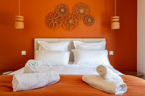 Chambre moderne de la villa La Loge Du Bassin aux murs orange, literie blanche, serviettes roulées et art mural décoratif