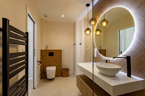 Salle de bain moderne à la Villa la Parenthese avec miroir rond illuminé, vasque blanche, porte-serviettes noir et finitions bois