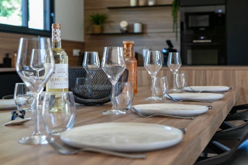 Mise de table élégante à la villa La Parenthèse à Andernos-les-Bains avec assiettes blanches, verres à vin et bouteille de Bordeaux