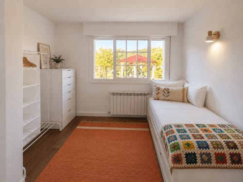 Acogedora habitación Nova Anduriña en Holibai con cama individual, muebles blancos, alfombra naranja y vistas al jardín