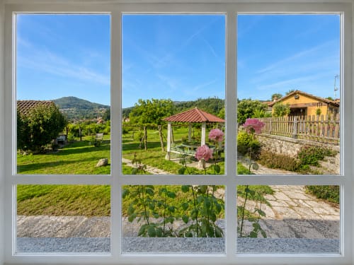 Vista de seis paneles del jardín de la casita Nova Anduriña en Holibai, Gondomar, con cenador, plantas floridas y sendero de piedra