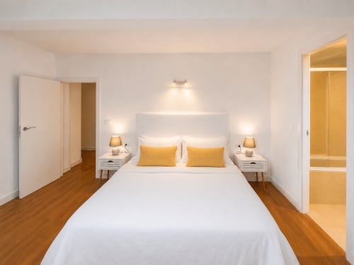 Dormitorio moderno en la casa rural Holibai Nova Anduriña en Gondomar con cama blanca, almohadas doradas, mesillas y suelo de madera