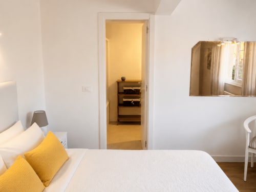 Dormitorio luminoso en la casita Nova Anduriña de Holibai, Gondomar, con cojines amarillos, ropa de cama blanca y acceso al armario