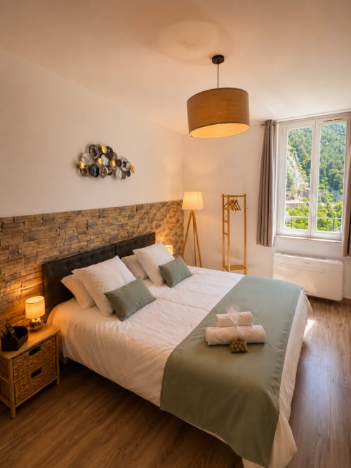 Cozy bedroom at Le Clos Androne in Sisteron with wooden headboard, white bedding, pendant lamp, and mountain views through