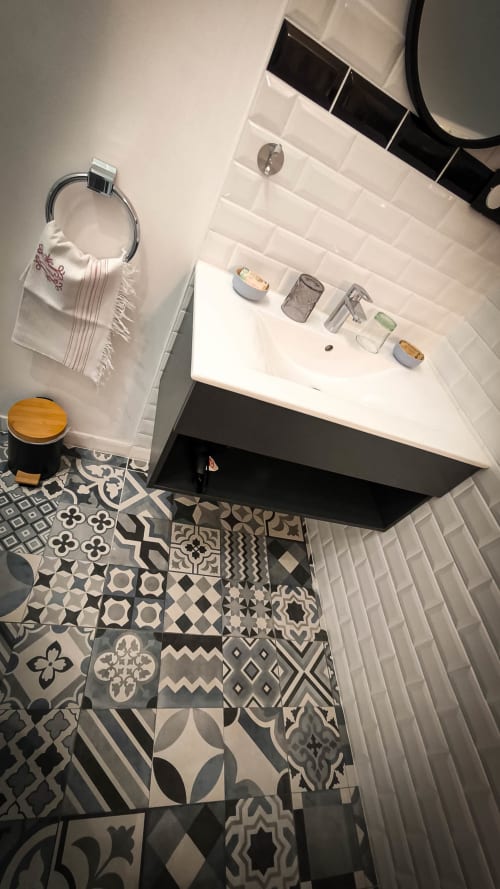 Salle de bains moderne du Clos du Buisson avec carrelage blanc, sol motifs, vanité noire et articles de toilette à Saint Aubin