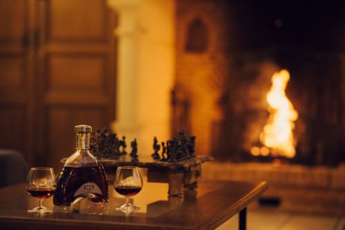 Cognac et verres près de la cheminée au Clos Céleste B&B à Étretat, avec un jeu d'échecs dans une douce lueur ambrée