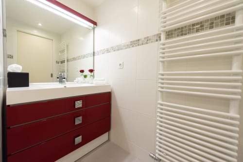 Salle de bain moderne au Clos Céleste avec vanité rouge, lavabo blanc, porte-serviettes chauffant et roses rouges décoratives à Ecrainville.