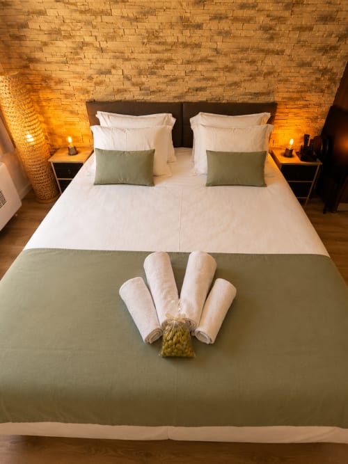 Luxury hotel bedroom at Le Clos Androne in Sisteron with twin beds, rolled towels, and ambient brick ceiling lighting