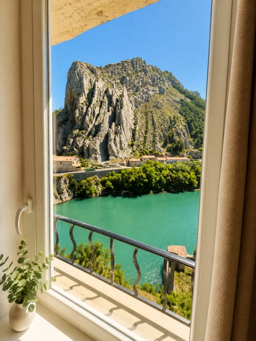 Window view from Le Clos Androne studio in Sisteron, France overlooking emerald Durance River and Rocher de la Baume cliff