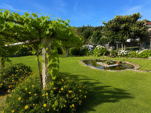Vista del exuberante jardín de la cabaña Holibai en Gondomar con estanque, flores amarillas, pérgola con enredaderas y césped cuidado
