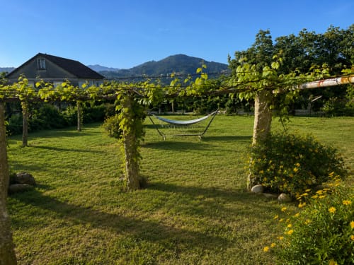 Exuberante jardín con hamaca entre postes, casa y montañas visibles en la casa rural Holibai en Gondomar