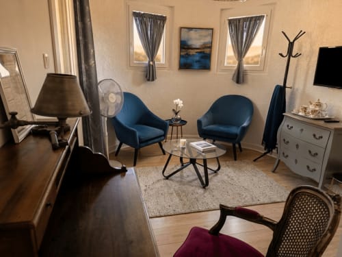 Chambre d'hôtel moderne à La Bastide Des Muriers avec fauteuils bleus, bureau en bois et vue sur le jardin
