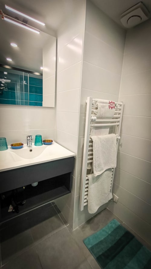 Salle de bains moderne au Clos du Buisson avec carrelage blanc, lavabo, miroir, sèche-serviettes chauffant et accents bleu-vert