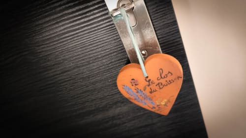 Porte-clé orange en forme de cœur avec texte manuscrit suspendu à un clip métallique au gîte Le Clos du Buisson à Saint
